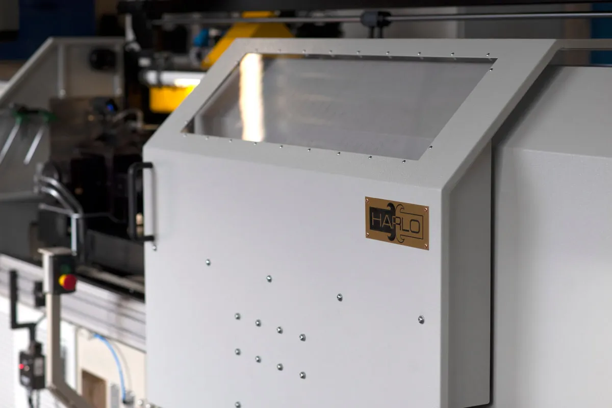 Friction welding machine enclosure with Harlo nameplate, the machine blurred behind it