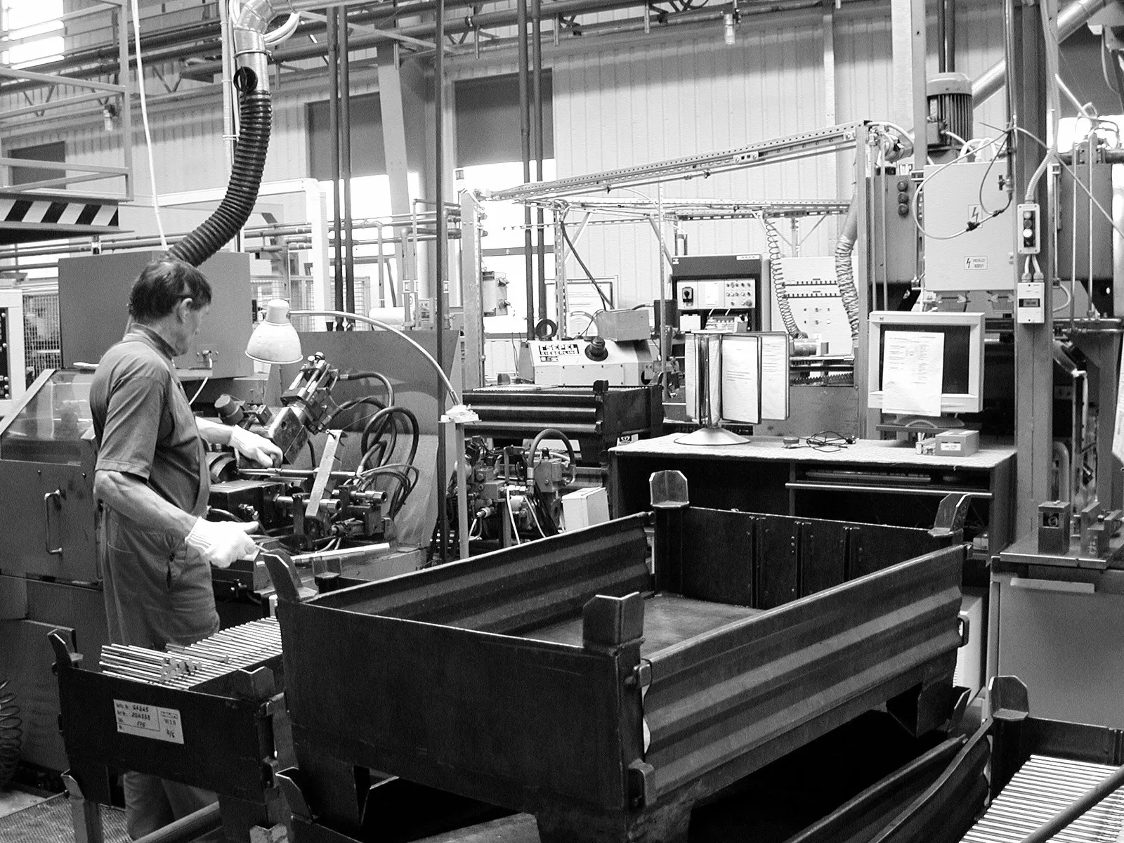 Friction welding machines in the production hall in 2000, with an operator and a workpiece rack in the foreground, archive photo